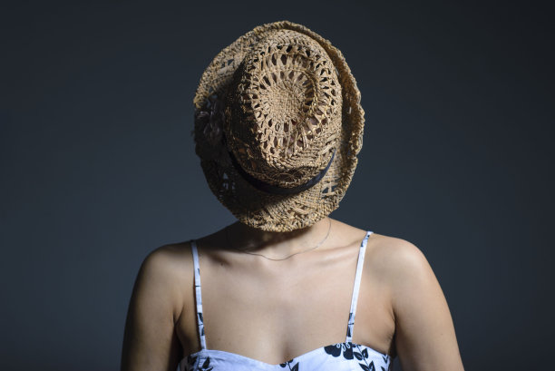 女孩脸上戴着草帽。草帽创意概念照片。灰色背景上的工作室照片图片下载
