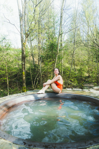 年轻女子在松林里的温泉池里放松图片下载