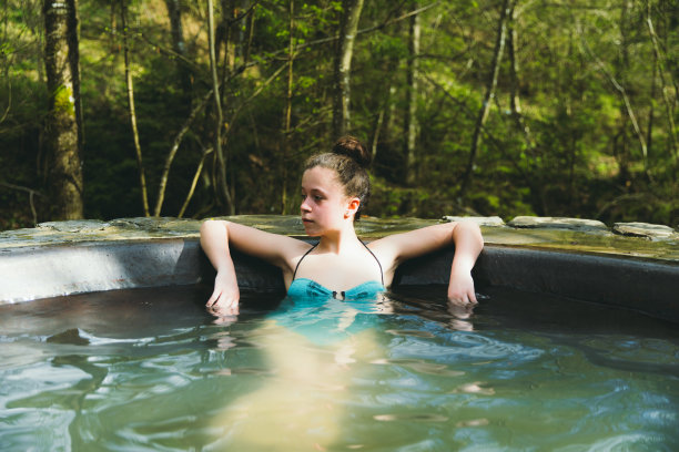 年轻女子在松林里的温泉池里放松图片下载