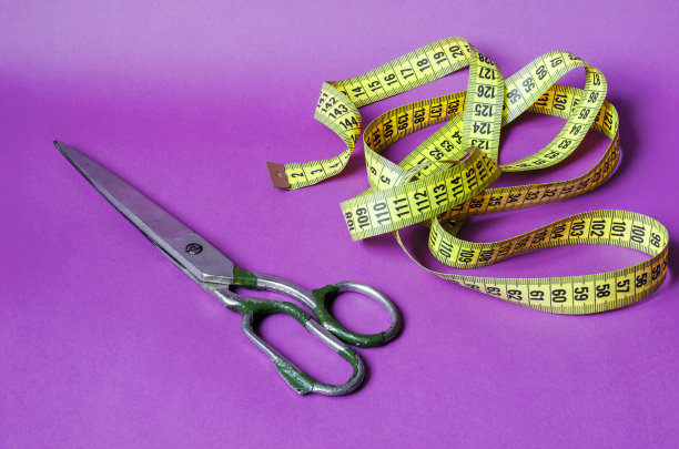 紫色背景上的旧金属剪刀和黄色卷尺。图片下载