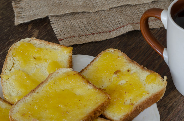 面包片和椴树蜂蜜在黑暗的木制背景。图片下载