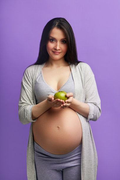 怀孕苗条的女人，大肚子抱着苹果孤立的蓝色墙图片下载