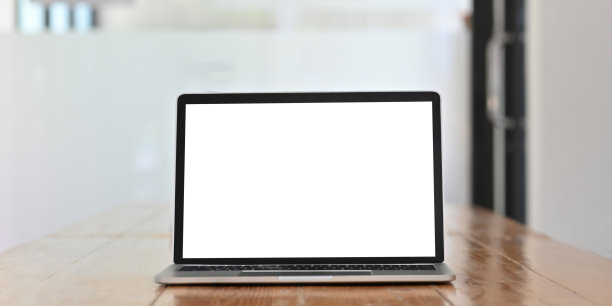 白色的空白屏幕电脑笔记本电脑放在木制的办公桌上，舒适的办公室玻璃墙作为背景。图片下载