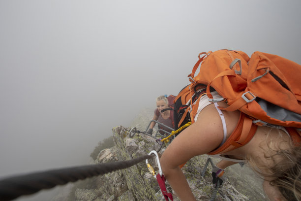 在雾中，一名年轻女子爬上via ferrata图片下载