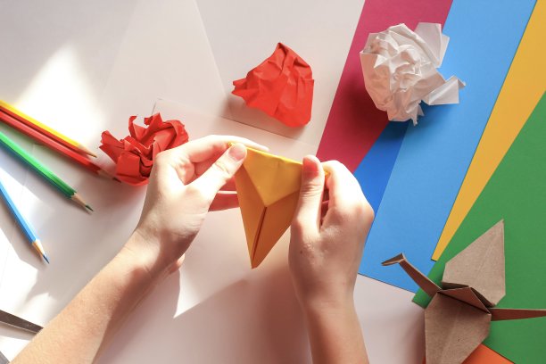 孩子们的手在白色的背景上用黄色的纸做折纸鹤。一步一步的折纸教程。孩子的创意观念，回到学校。图片下载