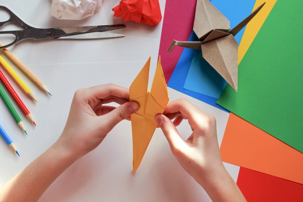 孩子们的手在白色的背景上用黄色的纸做折纸鹤。一步一步的折纸教程。孩子的创意观念，回到学校。图片下载