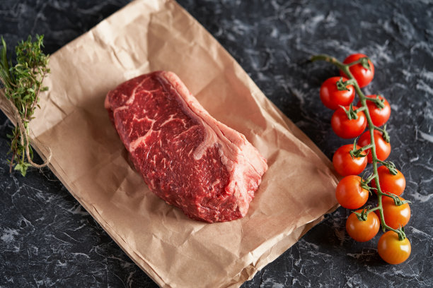 新鲜，调味多汁的纽约牛排在食物纸上，西红柿在一个黑色的结构背景上的小树枝上。餐厅菜单，传统的美国烧烤食谱图片下载