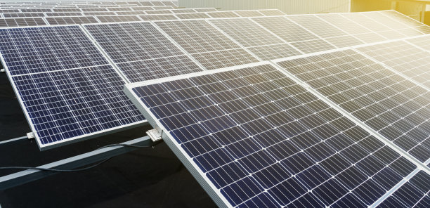 太阳太阳能电池板在地面上，太阳照射右侧。横幅照片。替代太阳能发电厂。地球的可持续性。绿色能源为家。蓝色电模块排成一排。图片下载