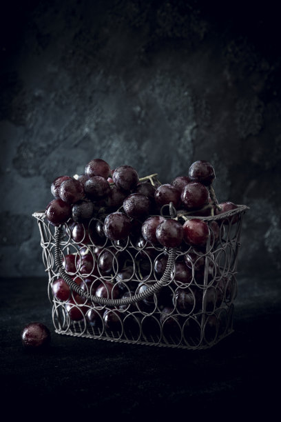 红色的葡萄在一个铁丝编织的篮子里的特写在黑暗的背景图片下载