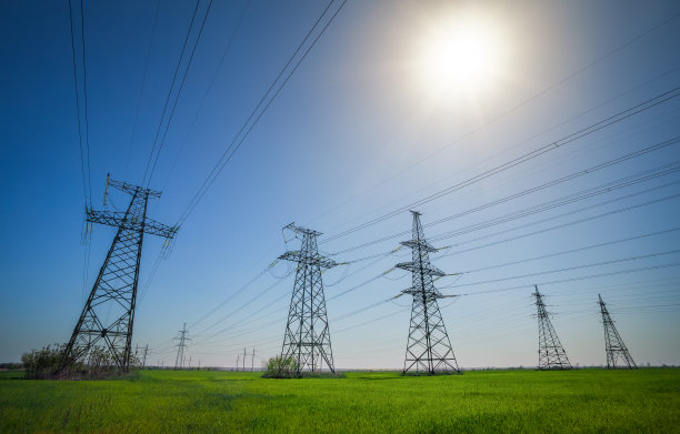 在一个晴朗的日子里，蓝天白云，在一个平坦的绿色农业景观中的高压电线和电力塔。图片下载