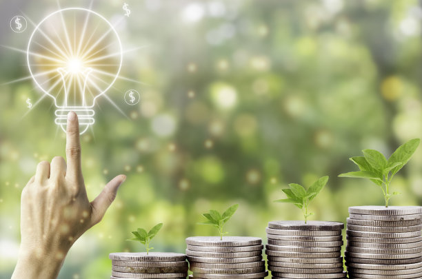 储蓄和投资的想法，人的手指触摸排列着银币的灯泡，树木生长在成堆的硬币在自然背景。储蓄、会计和财务概念。图片下载