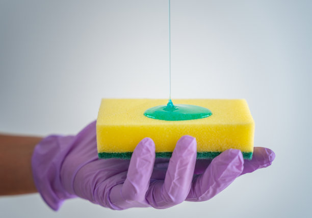 一只戴着紫色手套的手拿着洗碗用的海绵，消毒剂从上面倾泻而出图片下载
