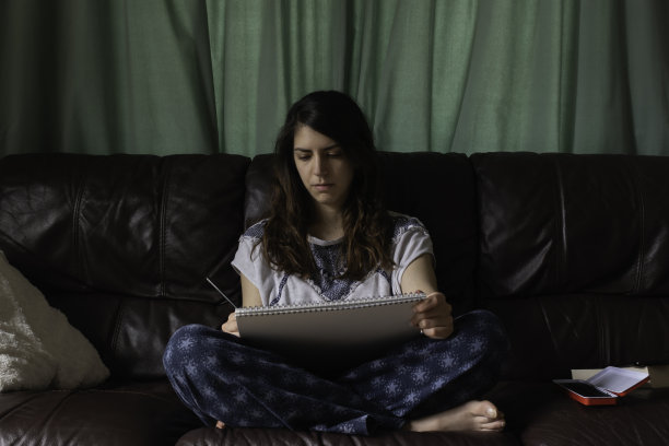 盘腿女士在她的皮沙发上画画，同时用铅笔画画图片下载