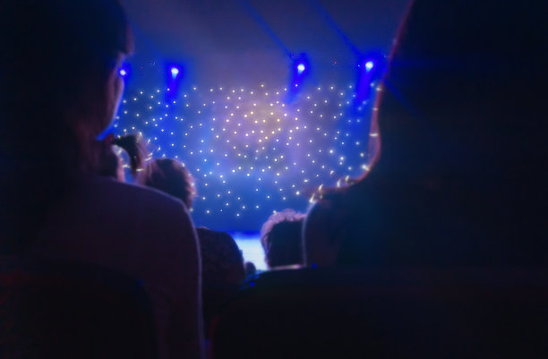观众背影模糊。在蓝光下从背后拍摄的剪影。闪闪发光的舞台灯光。投影仪在黑暗中。激光和灯光表演。舞台上模糊不清的灯光小景深。图片下载