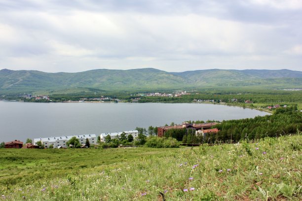 伟大的全景。一个泻湖和一个干净的山湖在雄伟的山脉中间在雾霾中。绿色的草，黄色和蓝色的花在前景图片下载