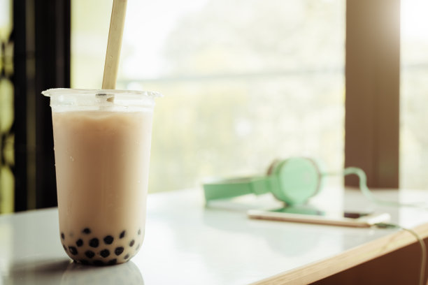 白色桌子上塑料杯装的泡泡茶，背景虚化图片下载