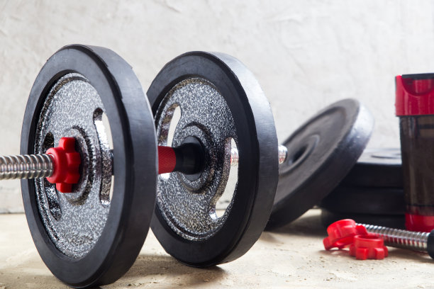 铁哑铃和乳清蛋白摇摇杯，健身或健美概念背景，灰色水泥地面上的产品照片图片下载