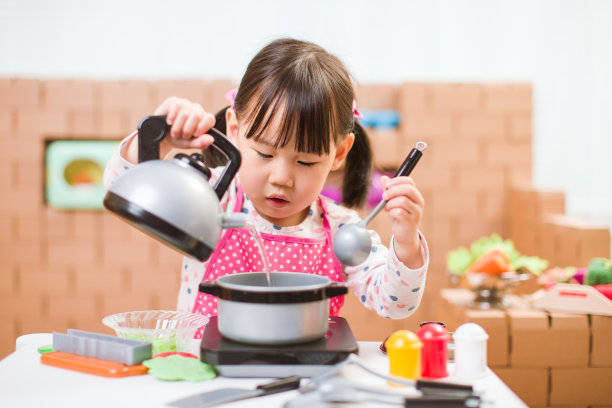 蹒跚学步的小女孩以纸板块为背景，假装扮演准备食物的角色图片下载