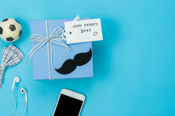 表顶视图父亲节节日背景概念。平板放置的礼物盒与配件对象的季节标志，手机，礼盒和耳机和贺卡上的蓝色纸。图片下载