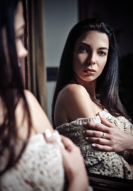 迷人的女孩站在镜子前。迷人的年轻女子的肖像图片下载