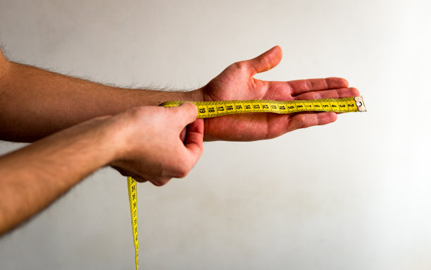 用黄色卷尺测量左手从手指到手腕的人。白色背景。橄榄肤色。图片下载