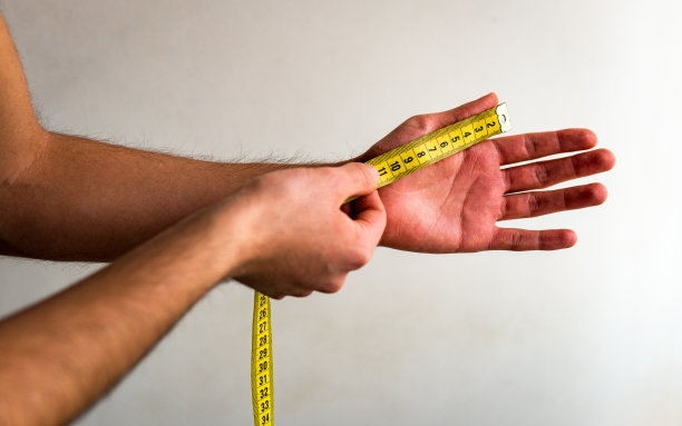 用黄色卷尺测量左手拇指的人。白色背景。橄榄肤色。图片下载