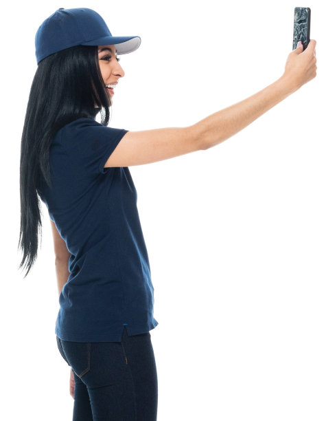 拉丁美洲和西班牙裔的年轻女性站在白色背景前，戴着棒球帽，使用手机拍照图片下载