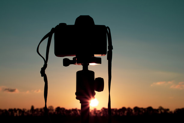 三脚架上的一台照相机的剪影，在草坪上拍摄红色的日落图片下载