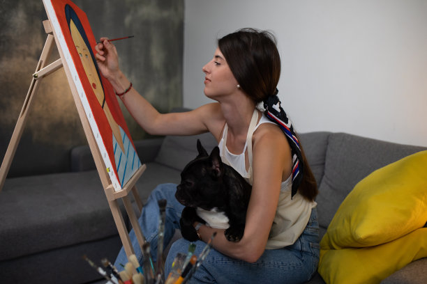 一个漂亮的年轻女子一边画一边抱着一只可爱的狗狗在她的腿上图片下载