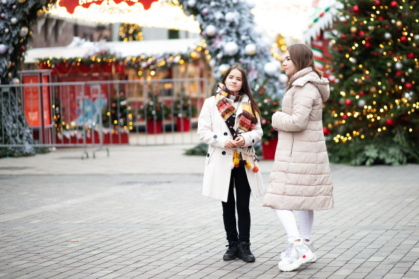 年轻女孩的闺蜜们在圣诞集市上相遇，在彩灯和圣诞树的背景下散步，聊天、讨论、欢笑。图片下载