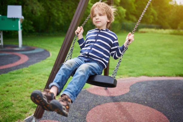户外肖像可爱的学前班欢笑的男孩荡秋千在操场上图片下载