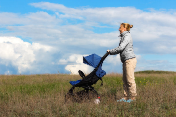 一位年轻的妇女正推着婴儿车带着一个孩子漫步在村庄的绿色草地上。图片下载
