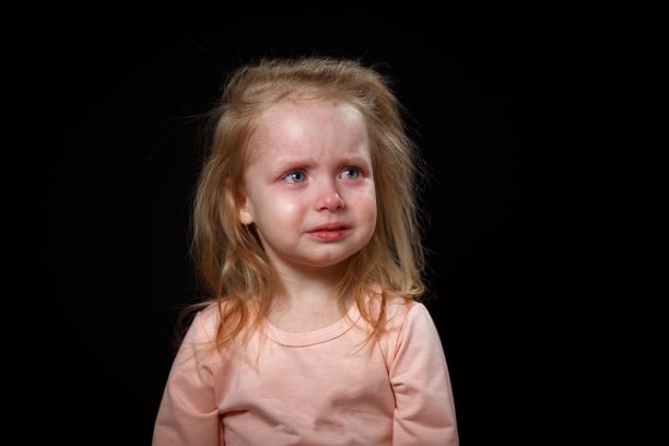 小女孩在大声哭，她很难过，她歇斯底里。她无法平静下来。照片在工作室在一个黑暗的背景。图片下载