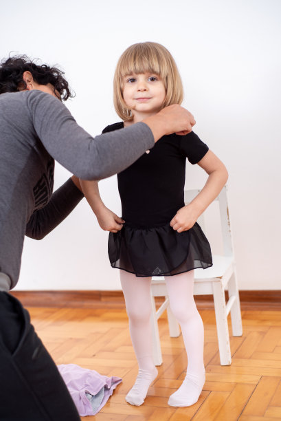 慈爱的母亲帮助她的小女儿在家庭芭蕾舞练习穿芭蕾服装-库存照片图片下载