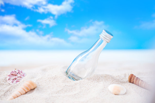 瓶子在沙滩上和贝壳在模糊的热带蓝色的海洋和清澈的蓝色天空图片下载