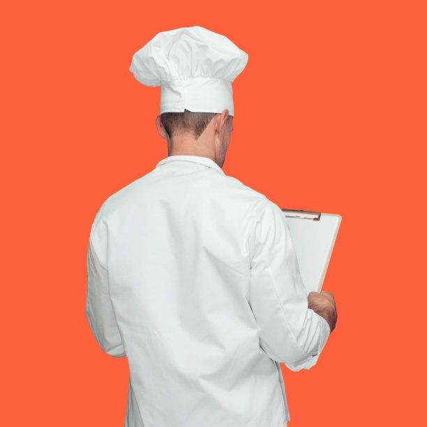 白人男厨师站在橙色背景，穿着制服，拿着文件图片下载