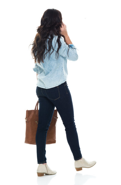 白人女性穿着牛仔裤走在白色背景前，拿着钱包和手机图片下载