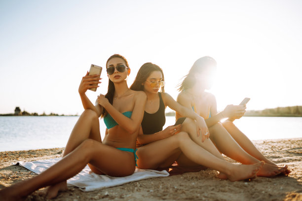 三个快乐的女孩朋友穿着泳衣在海滩上自拍。图片下载