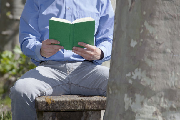一个商人坐在公园的长椅上读一本绿皮书——专注于这本书图片下载