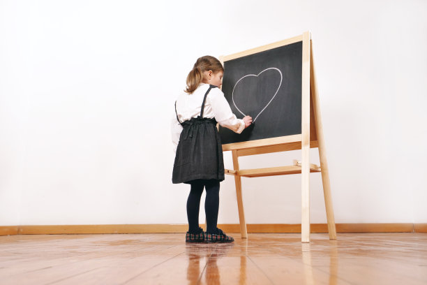 一个快乐的小女孩扮成老师站在小黑板前，讲授经济学、市场营销、团队合作和数学。图片下载