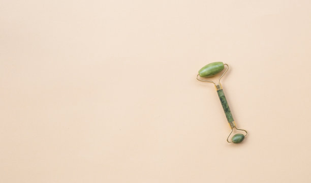 面部按摩疗法。绿色玉石面按摩器，浅米色背景。平铺，拷贝空间，俯视图。女性放松的气氛。图片下载