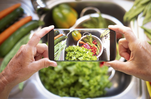 一位女士用手机拍了一张手把蔬菜洗干净的照片。各种新鲜的素食和素食食品绿色，红色和橙色图片下载