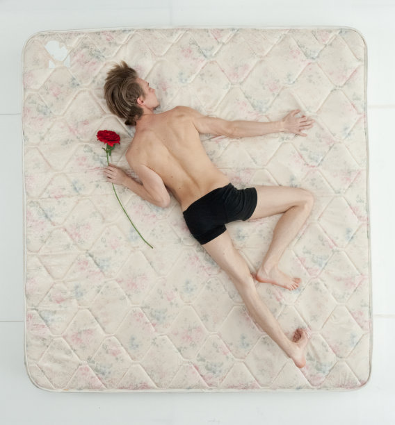 年轻男子穿着内衣，手捧鲜花，在卧室的白色背景前放松图片下载