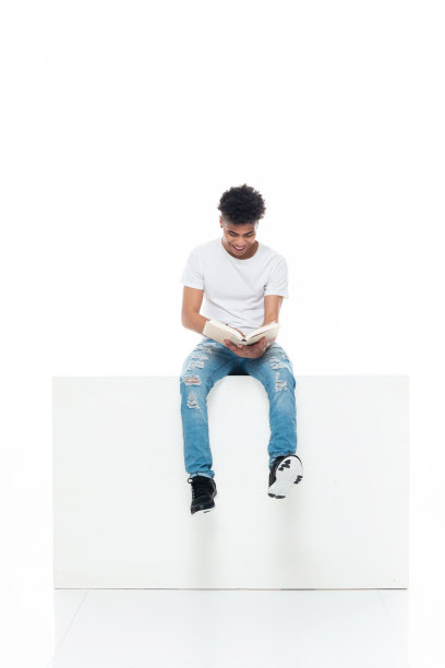 非裔美国男大学生穿着运动鞋，拿着课本坐在白人背景前图片下载