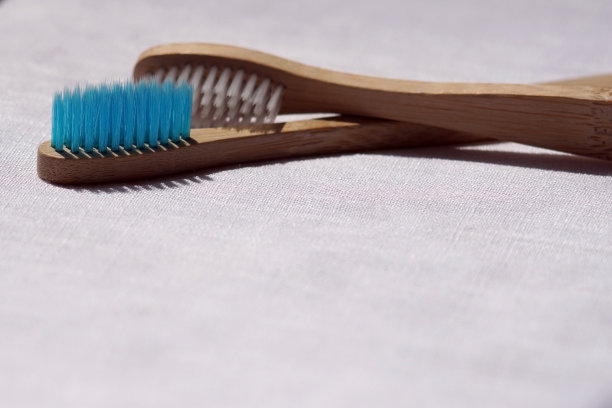 这是一个环保的白色和蓝色竹子牙刷的特写，在白色亚麻的背景上。天然有机浴室美容产品概念。本空间图片下载