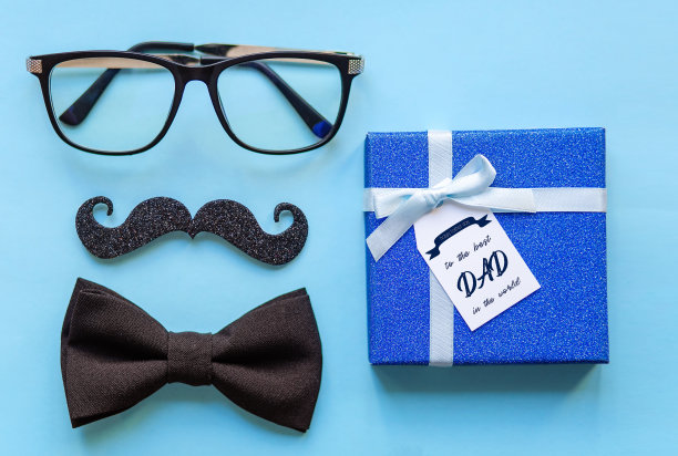 特写的眼镜，胡子，领带和上面刻着“祝世界上最好的爸爸父亲节快乐”的礼物在蓝色的背景上。图片下载