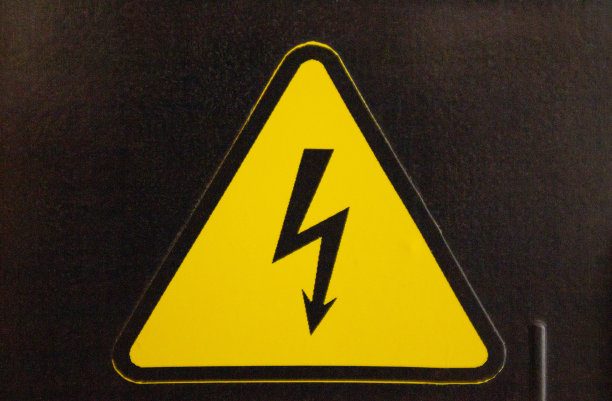 黑色的墙上有黄色的危险标志。黄色三角形中的黑色闪电。图片下载