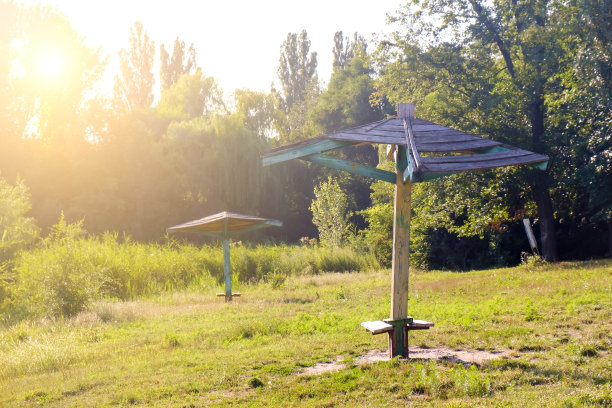 在一个阳光明媚的夏日日落时分，在一个废弃的、长满草和芦苇的河边海滩上，两把古老的木制沙滩伞。图片下载