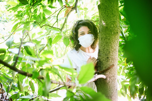 微笑的妇女与保护面罩在树叶和绿色植物图片下载