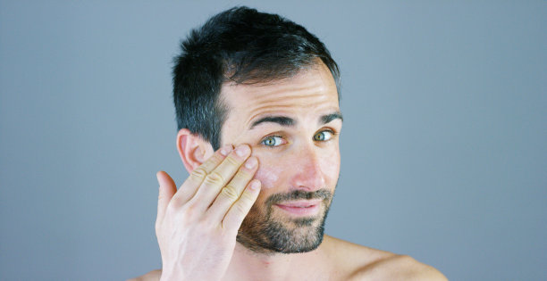 一个非常英俊的男人微笑着用面霜和眼部轮廓抗皱抗衰老来照顾自己的身体，懂得美丽。图片下载